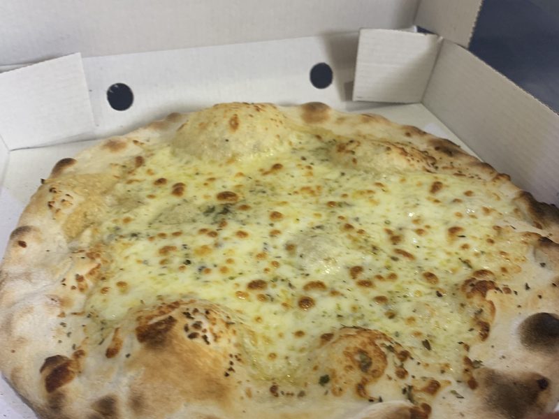 A round focaccia with melted mozzarella, garlic and oregano in an open takeaway box