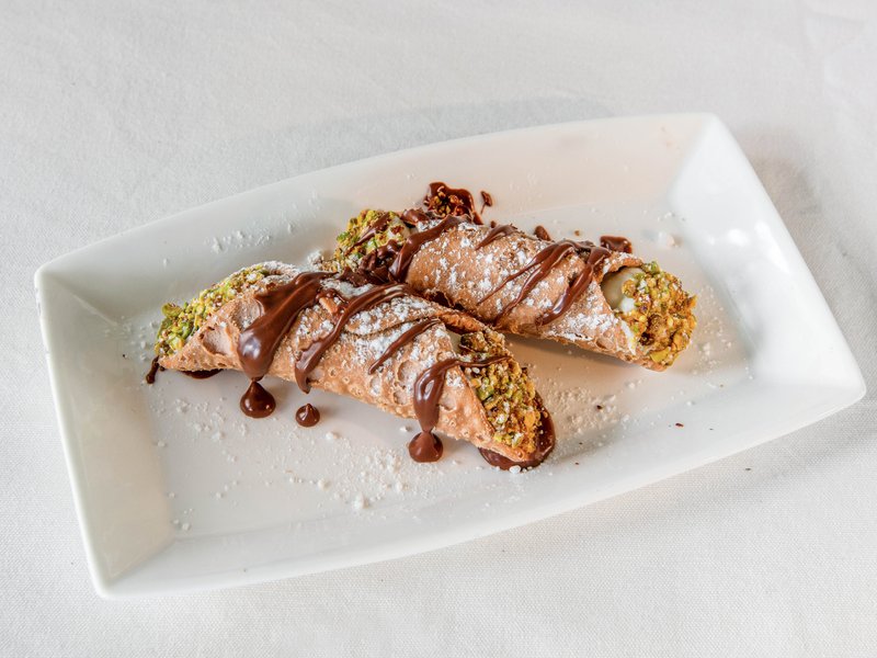 Two cannoli filled with ricotta, dusted with icing sugar and finished with chocolate and pistachio