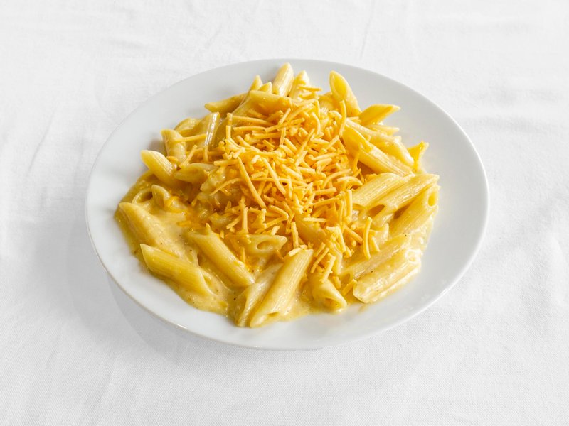 A plate of penne in a cheese sauce, topped with grated cheddar
